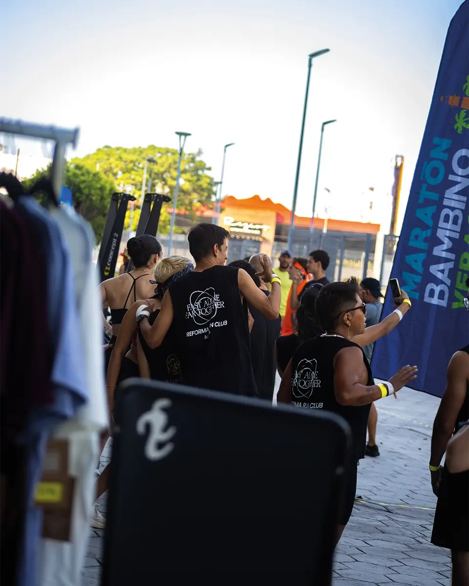 Corredores del club conviviendo junto a los toldos del Maratón Bambino, con la ropa colgada en un perchero en primer plano.