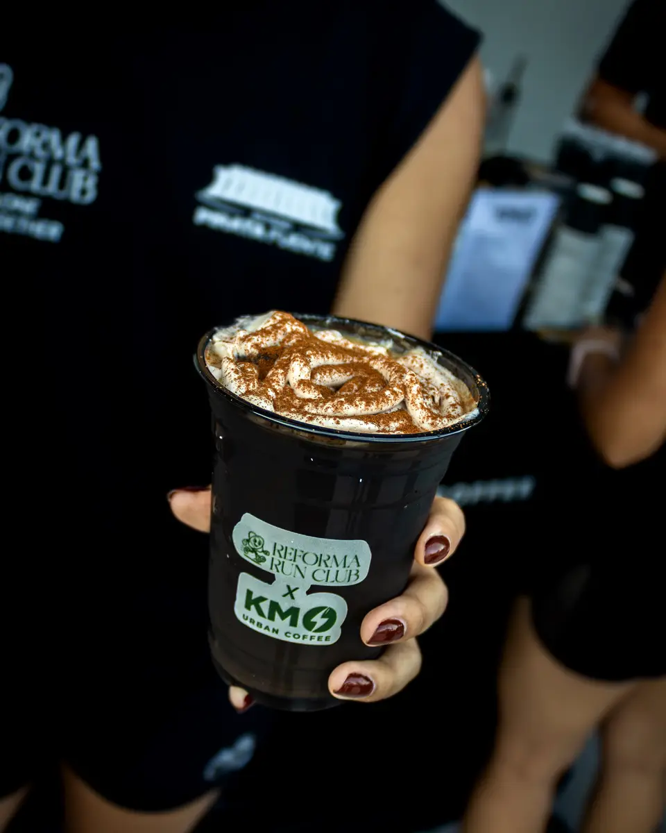 Unas manos sostienen un vaso de café con el sello de Reforma Run Club y Km0 Coffee, al terminar la corrida.