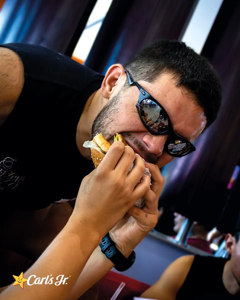 Primer plano de un corredor con lentes de sol dando una mordida grande a su hamburguesa.