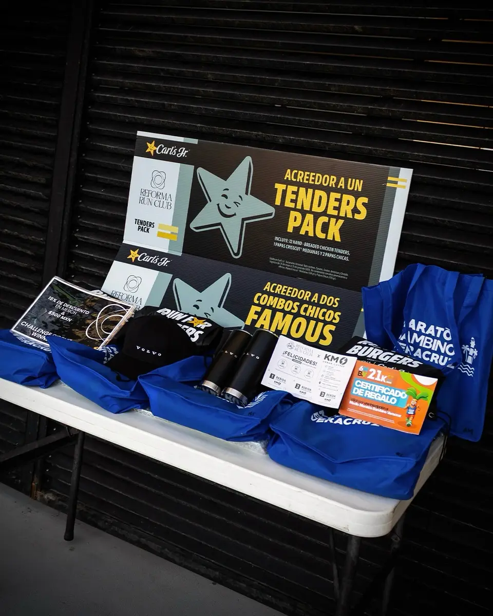 Mesa de premios del evento: vales de Carl's Jr., playeras azules y tarjetas de las marcas aliadas.