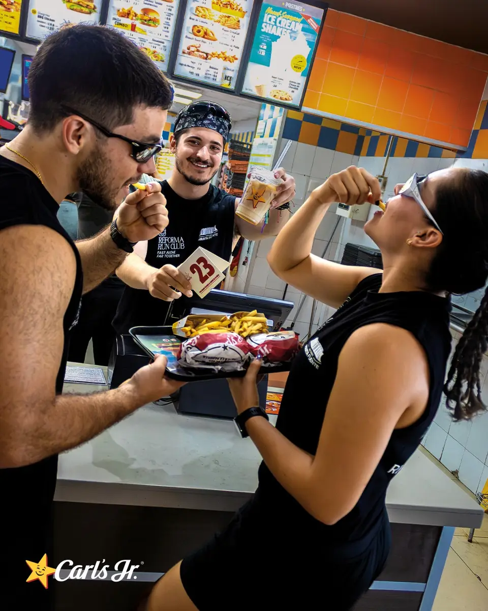 Tres corredores del club, de negro, brindan con vasos y una charola de papas en el mostrador de un Carl's Jr. después de la corrida.